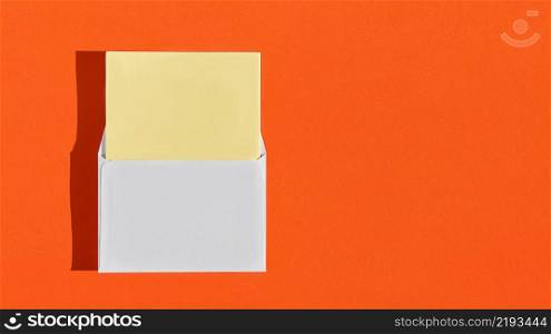 Postcard mockup with white envelope and blank yellow writing paper on orange burnt background. Creative concept, greeting card template. Horizontal layout with copy space