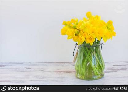 Posy of bright yellow daffodils on white wooden table wih copy space. Narcissus in vase