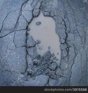 Pot hole or pothole image of a broken cracked asphalt pavement with a dirty water puddle as a transportation symbol of road maintenance and the car insurance risk to auto suspensions.