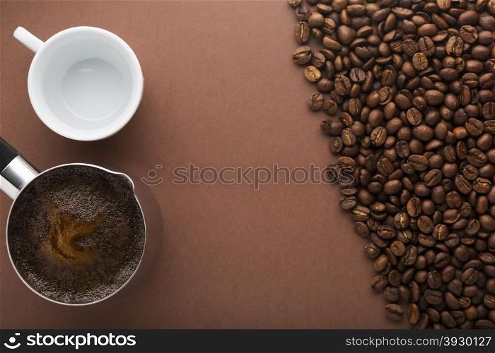 Pot of coffee, coffee beans and white empty cup on brown background. Top view. Focus on pot