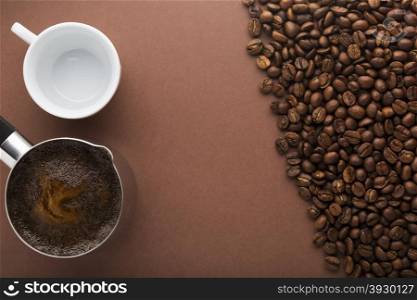 Pot of coffee, coffee beans and white empty cup on brown background. Top view. Focus on pot