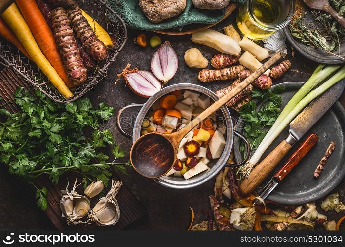 Pot with sliced colorful vegetables and cooking spoon on dark rustic table background with organic vegetarian ingredients and kitchen tools , top view. Healthy and clean food and eating concept.