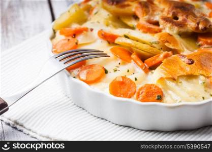 Potato and carrot gratin with herbs in bowl
