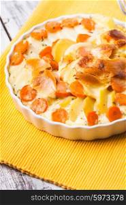 Potato and carrot gratin with herbs in bowl. Potato and carrot gratin