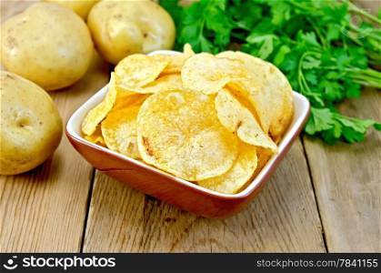 Potato chips in a clay bowl, fresh potatoes, parsley on a wooden boards background