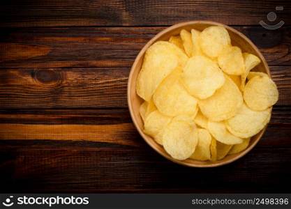 Potato chips in bowl on dark wooden table