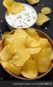 Potato chips in bowl with sauce dip on dark table