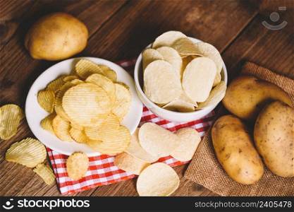 Potato chips snack on bowl and plate, Crispy potato chips on the kitchen table and fresh raw potatoes on wooden background