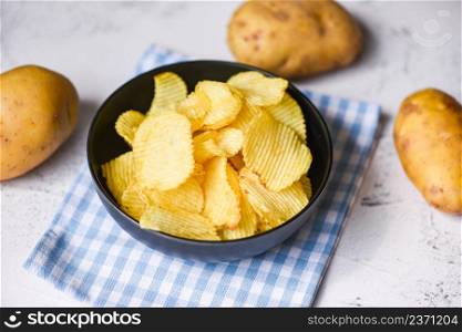 Potato chips snack on bowl, Crispy potato chips on the kitchen table and fresh raw potatoes on table background