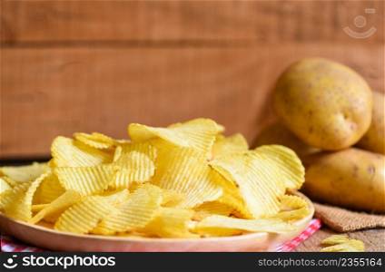 Potato chips snack on plate, Crispy potato chips on the kitchen table and fresh raw potatoes on wooden background