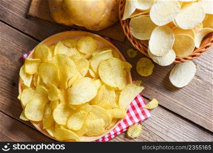 Potato chips snack on plate, Crispy potato chips on the kitchen table and fresh raw potatoes on wooden background - top view