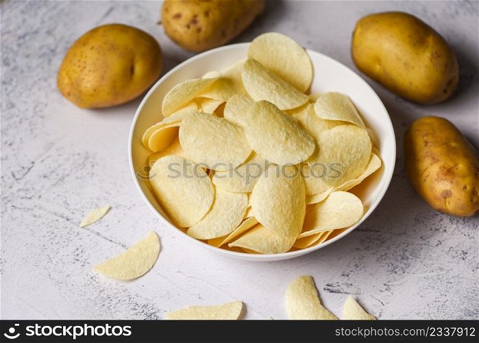 Potato chips snack on white bowl, Crispy potato chips on the kitchen table and fresh raw potatoes