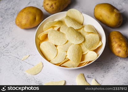Potato chips snack on white bowl, Crispy potato chips on the kitchen table and fresh raw potatoes