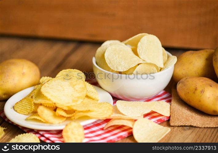 Potato chips snack on white plate, Crispy potato chips on the kitchen table and fresh raw potatoes on wooden background