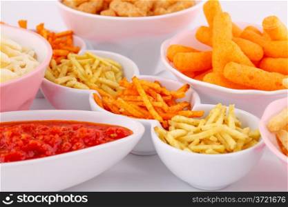 Potato, corn and wheat chips in bowls and red sauce isolated on gray background.