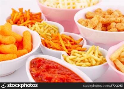 Potato, corn and wheat chips in bowls and red sauce isolated on gray background.