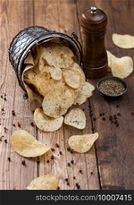 Potato crisps chips crunchy snack with black pepper in steel  bucket on wooden table background with mill and ground pepper.