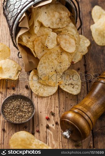 Potato crisps chips snack with black pepper in steel bucket on wooden table background with mill and ground pepper. Top view. Macro