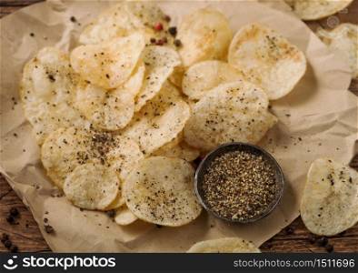 Potato crisps chips with black pepper taste on paper with ground pepper on wooden table background.