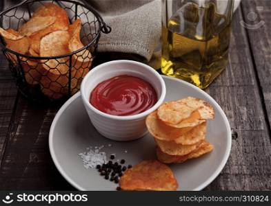 Potato crisps with ketchup on plate and olive oil. Wooden background