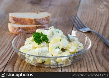 Potato salad in a glass bowl on wooden board. Potato salad in a glass bowl on wooden board.