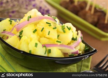 Potato salad with onions prepared in Swabian-Style (Southern Germany) garnished with chives, meatballs in the back (Selective Focus, Focus one third into the bowl)