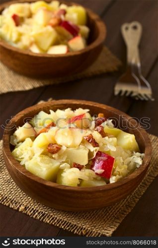 Potato, sauerkraut and apple salad with fried bacon served in wooden bowls, photographed with natural light (Selective Focus, Focus in the middle of the first salad)