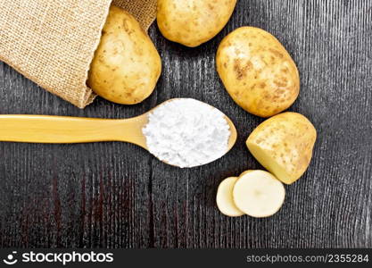 Potato starch in a spoon, vegetable tubers in a bag and on the table against the background of wooden board from above