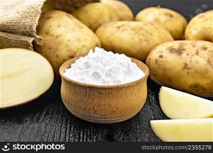 Potato starch in bowl, vegetable tubers in a bag and on a table against the background of black wooden board