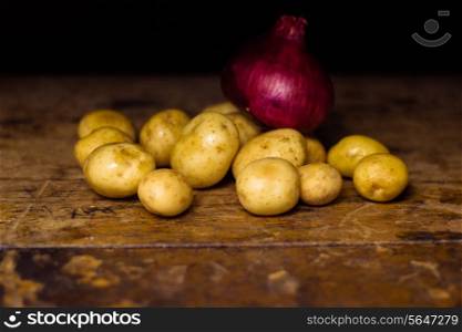 Potatoes and onion on wooden surface