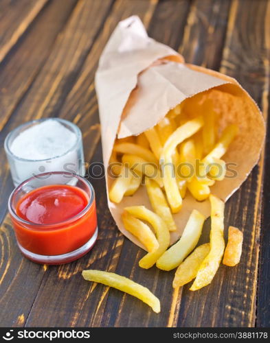 Potatoes fries in a little white paper bag on tomato sauce in bowl