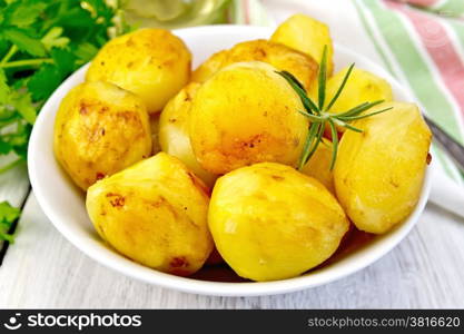 Potatoes roasted with rosemary in a white plate, napkin, parsley, oil, fork on the background of bright wooden planks