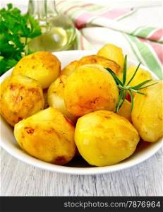 Potatoes roasted with rosemary in a white plate, napkin, parsley, vegetable oil on a background of pale wooden plank