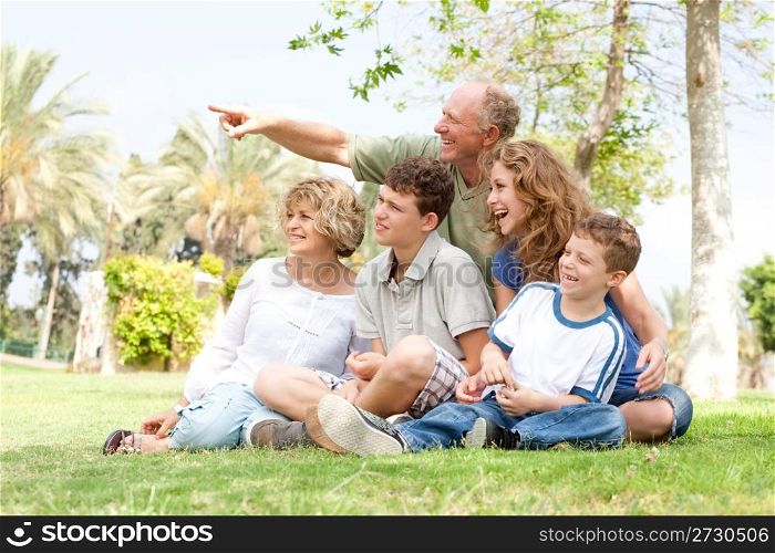 potrait offamily sitting in a park and grandfather pointing with his finger