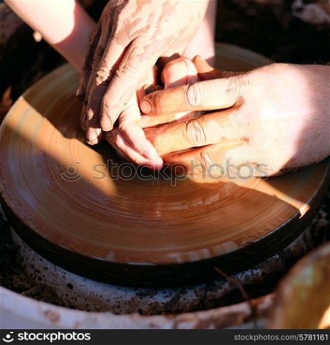 Potter&rsquo;s hands guiding child&rsquo;s hands to help him to work with the pottery wheel