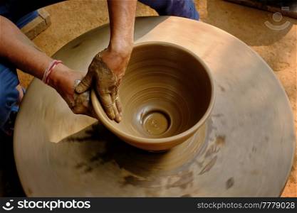 Pottery - skilled wet hands of potter shaping the clay on potter wheel. Pot, vase throwing. Manufacturing traditional handicraft Indian bowl, jar, pot, jug. Shilpagram, Udaipur, Rajasthan, India. Indian potter hands at work, Shilpagram, Udaipur, Rajasthan, India