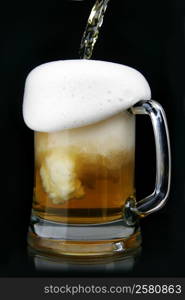 Pouring beer into mug over black background