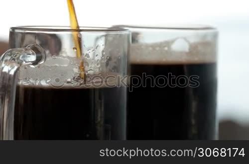 Pouring black beer into a beer cup close to another already full