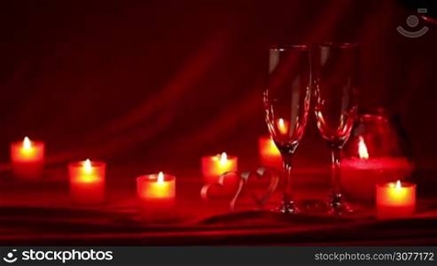 Pouring champagne in glasses at Valentines day celebration, still life with candles, roses and hearts on red silk