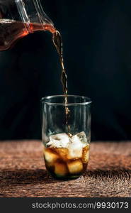 Pouring cold brew iced coffee in glass cup with ice cubes