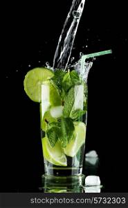 Pouring fresh mojito cocktail in glass isolated on black background