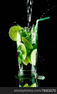 Pouring fresh mojito cocktail in glass notion ice splashing isolated on black background. Pouring mojito cocktail