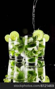 Pouring fresh mojito cocktail in glasses isolated on black background