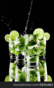 Pouring fresh mojito cocktail in glasses isolated on black background. Pouring mojito