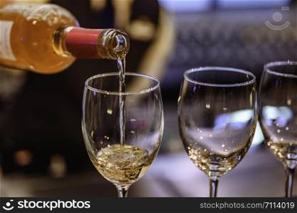 Pouring glasses of white wine from a bottle.