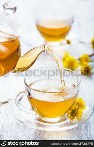 pouring herbal tea with coltsfoot flowers
