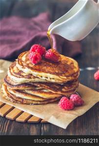 Pouring maple syrup on stack of pancakes with fresh raspberries