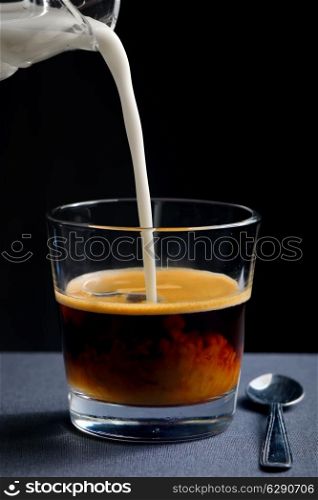 Pouring milk into a glass of black coffee. Isolated on black