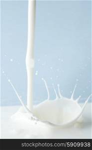Pouring milk splash on blue background close-up. Pouring milk splash