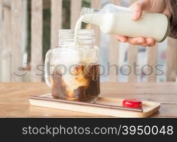 Pouring milk to iced glass of coffee, stock photo
